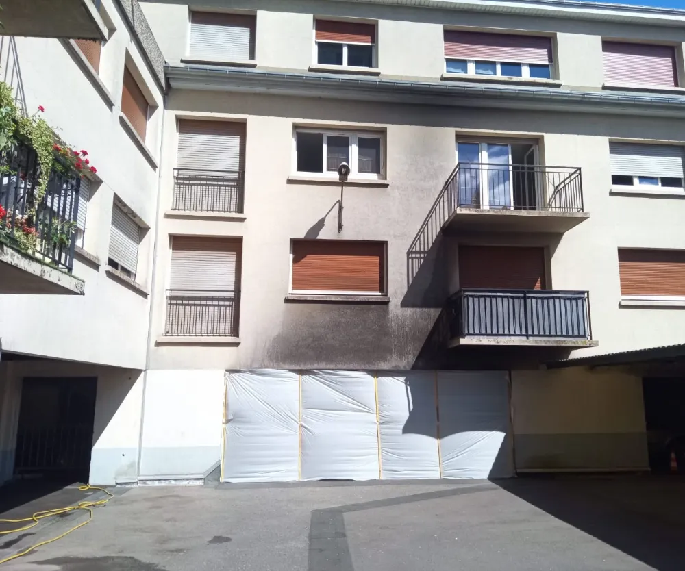 Façade d'immeuble noircie par les suies au-dessus d'un parking, avant intervention